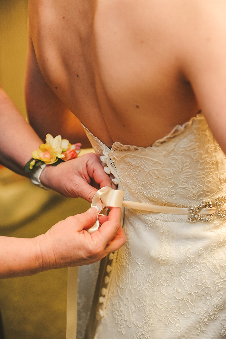 closeup of hands tying a ribbon on a wedding dress