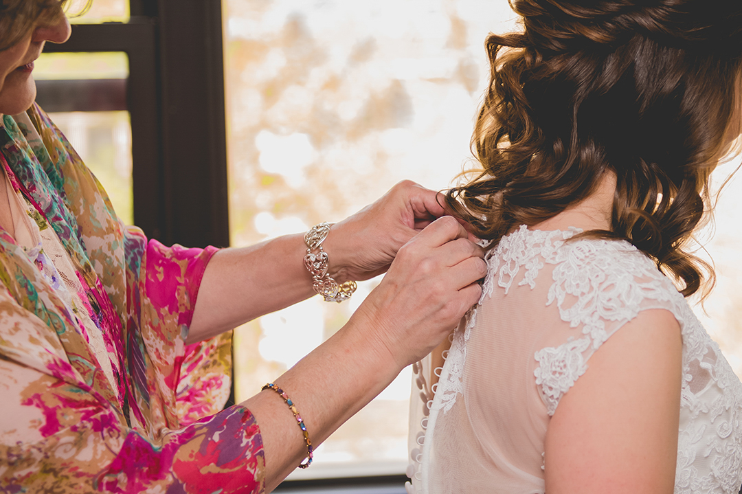 close up of the mother of the bride buttoning the dress of her daughter on her wedding day