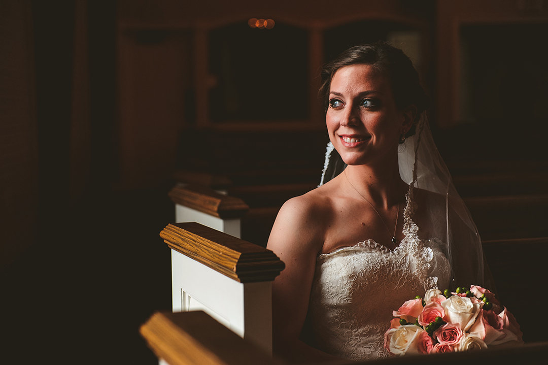 bride looking towards a stained glass window while sitting in her wedding dress