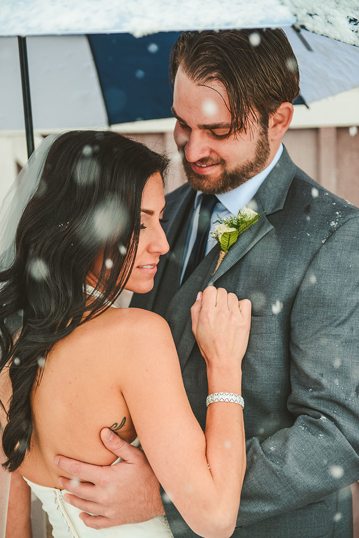a husband looks at his wife as the snow falls down at their County Line Orchard Wedding