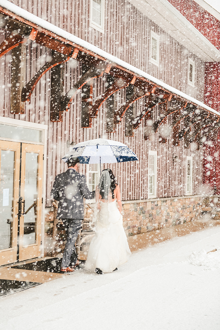 a husband holds an umbrella for his wife as the snow falls down