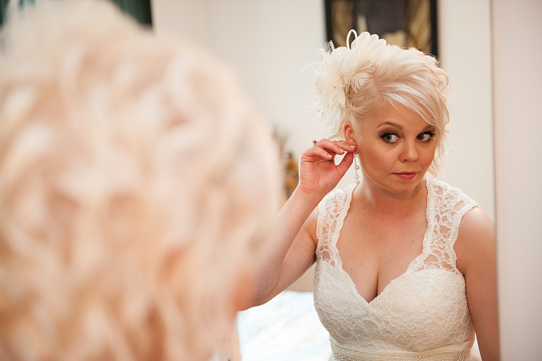 a bride looking into the mirror as she puts on her ear rings 