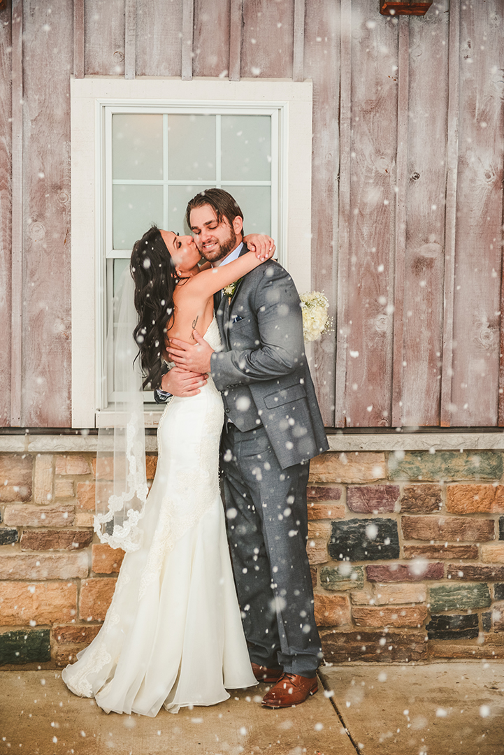 a woman hugs her husband in front of a rustic barn