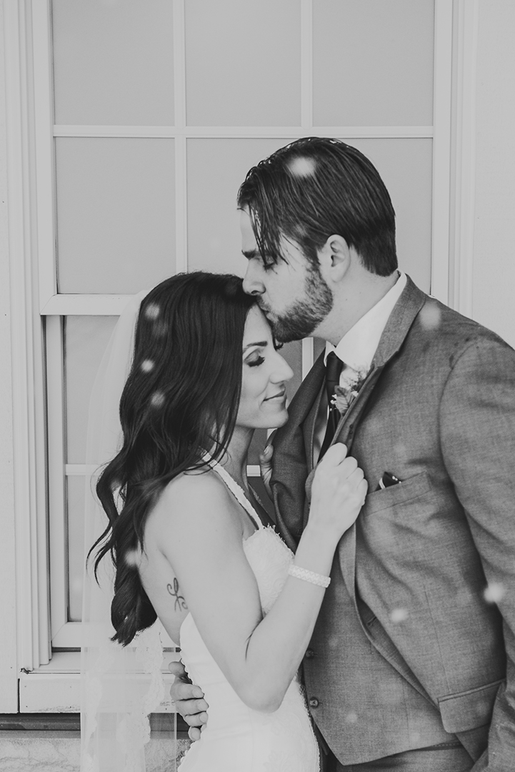 a husband and wife sneak a kiss on their wedding day outside in the snow