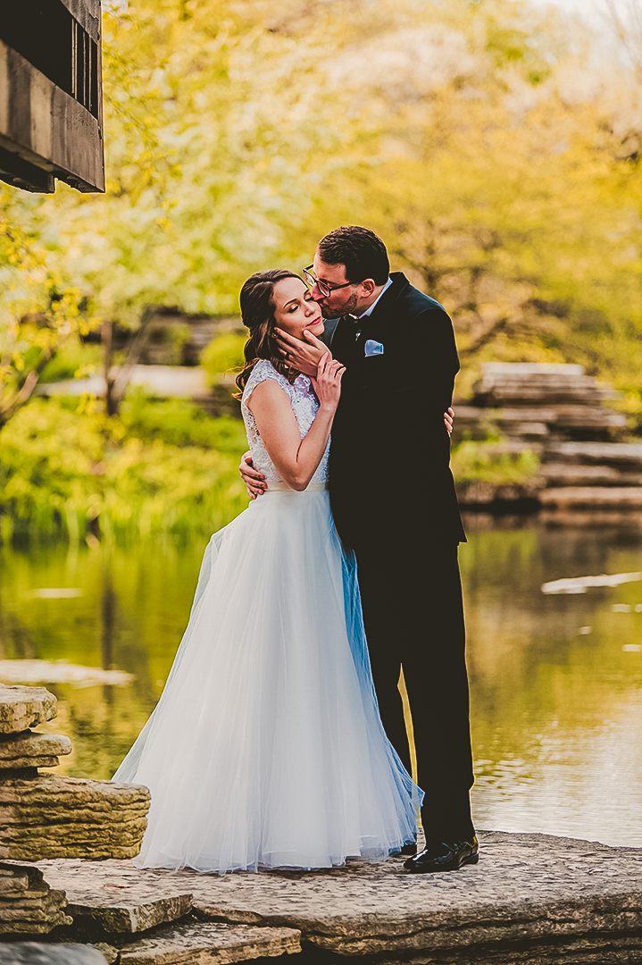 groom kissing brides cheek in front of a pond