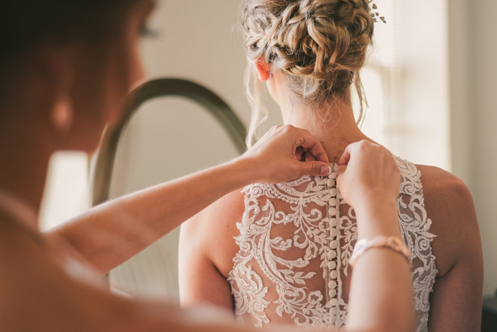 a maid of honor buttoning a brides dress at a Public Landing Restaurant Wedding