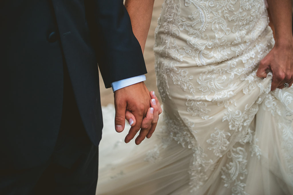 A close up photo of a bride and groom holding hands on their fall wedding day.