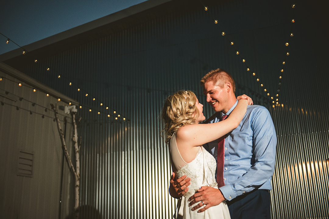 bride and groom stand in front of a vintage building at night with string lights overhead