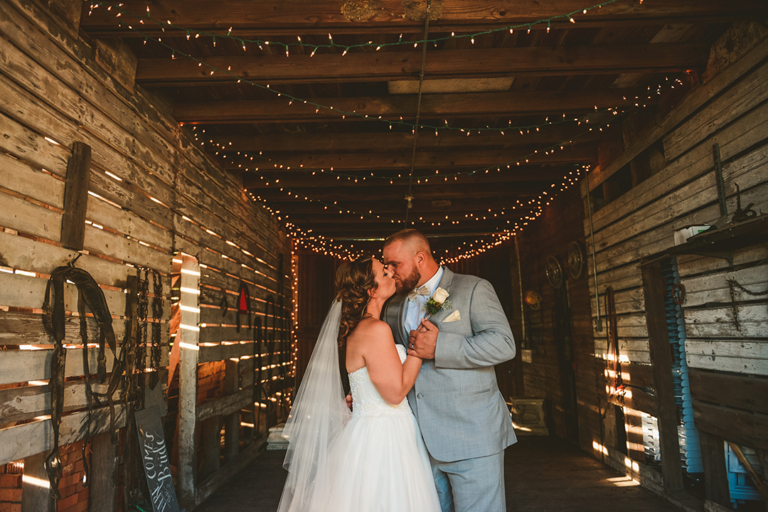 Bride and groom kissing in a barn with natural light and farm items around