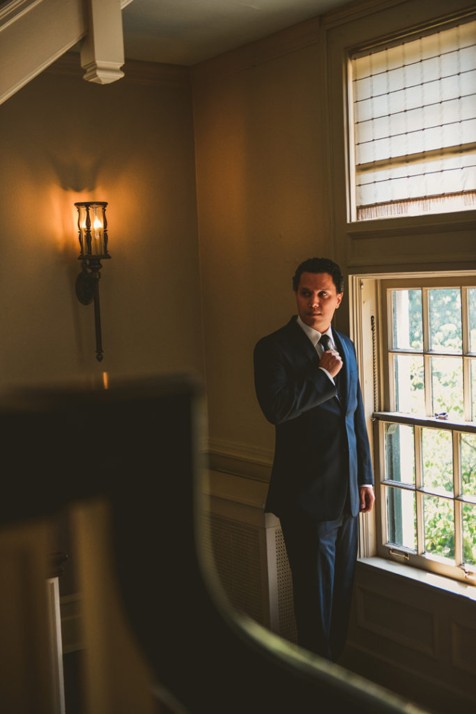 a groom fixing his tie in front a window at a Chaney Mansion Wedding