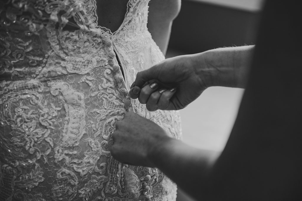 close up of a maid of honor zipping up a brides dress in Naperville