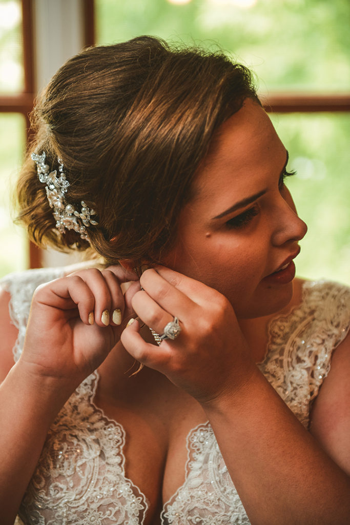 a bride smiling as she puts on her ear rings