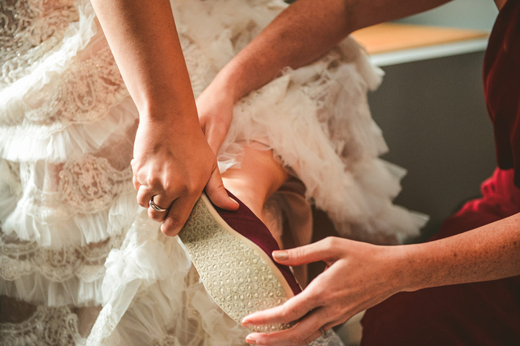 a maid of honor helping the bride put on her wedding shoes in Naperville