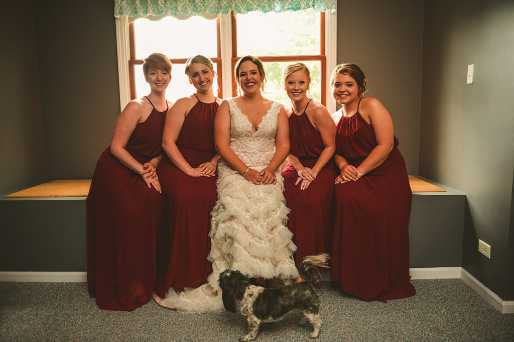 a bride and her bridesmaids laughing with the brides dog at their feet