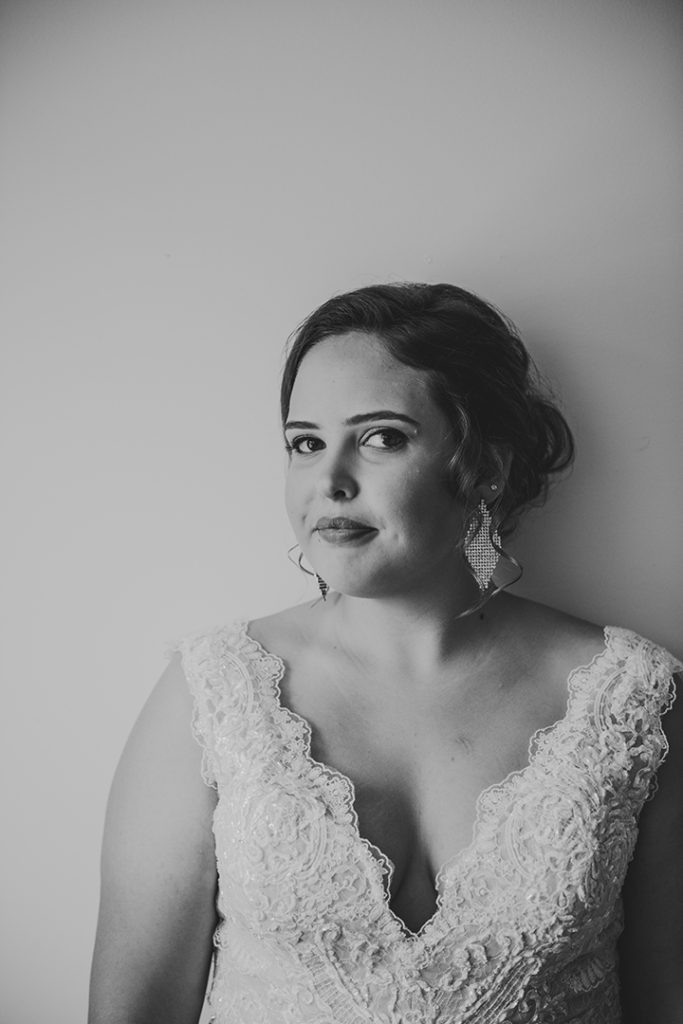 a bride smirking at camera in her wedding dress by a white wall