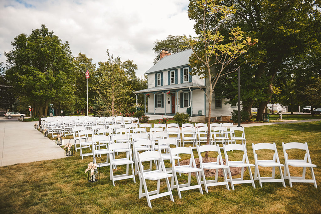 rows of chairs set up by a old house with a cloudy sky