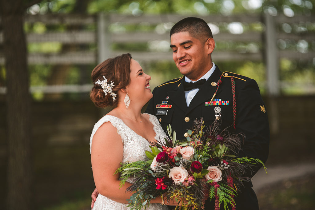 newlyweds laughing as they look at each other with a white farm fence in the background