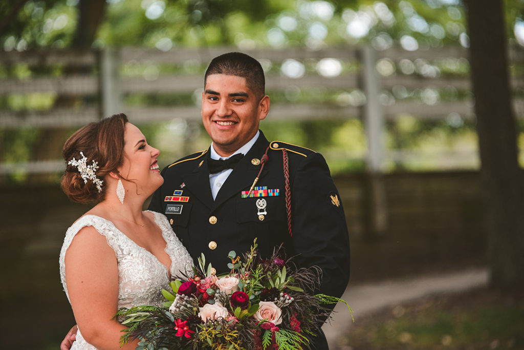 a groom looking at the camera as his wife looks at him with a big smile