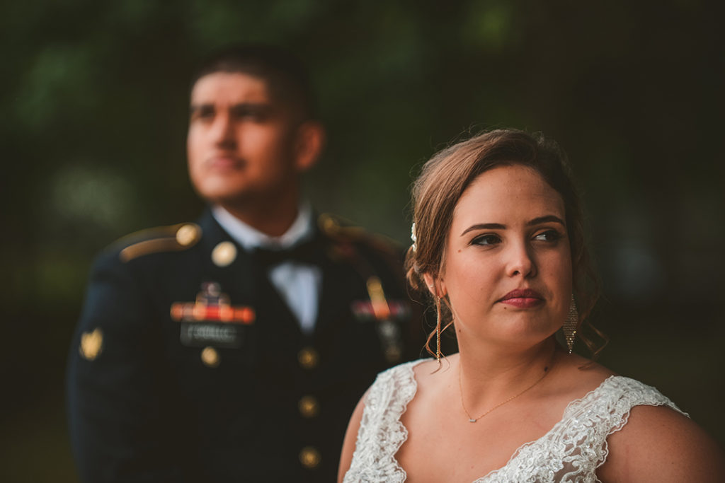 a serious bride looking into the woods as her groom stands behind her