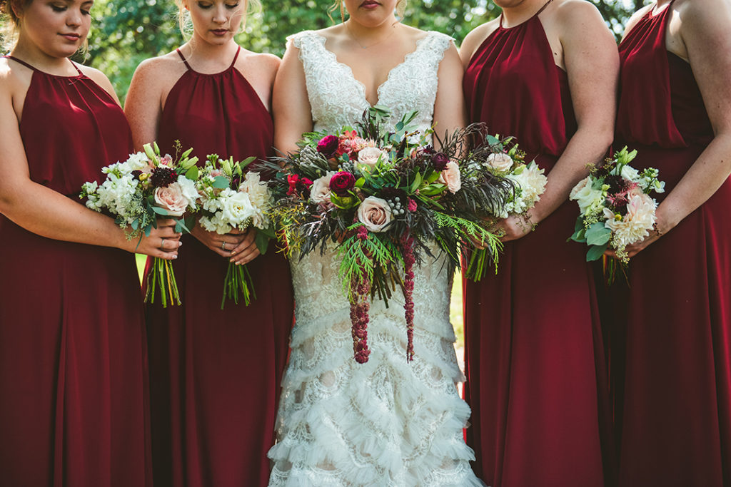 a detail image of bridesmaids in maroon dresses holding their real flower bouquets 