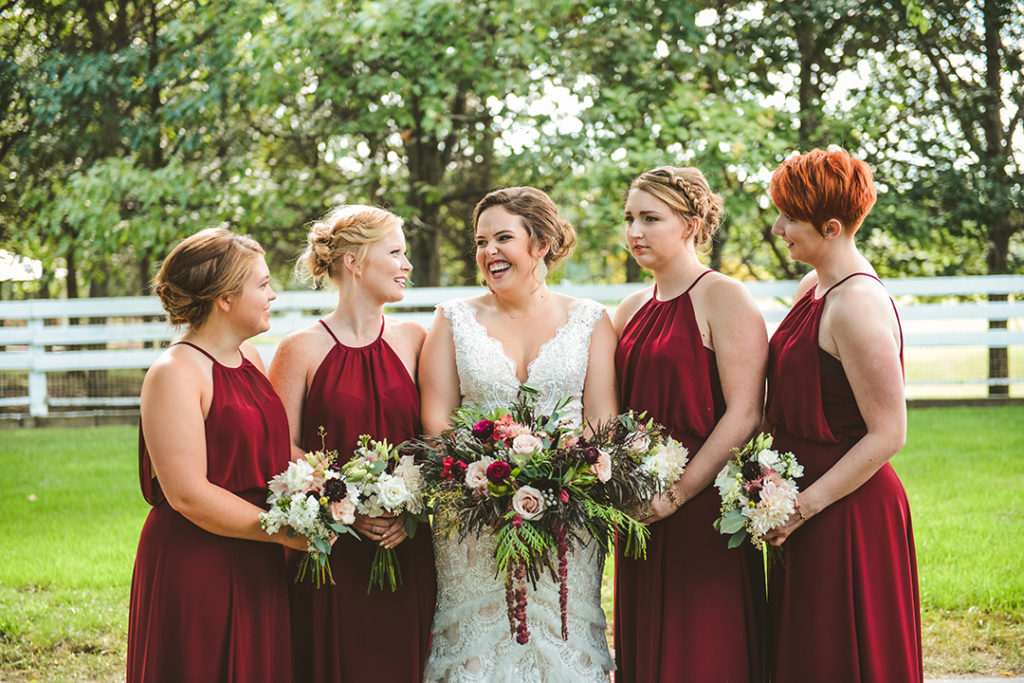 a bride laughing at her bridesmaids as they hold their bouquets at a park in Olympia Fields
