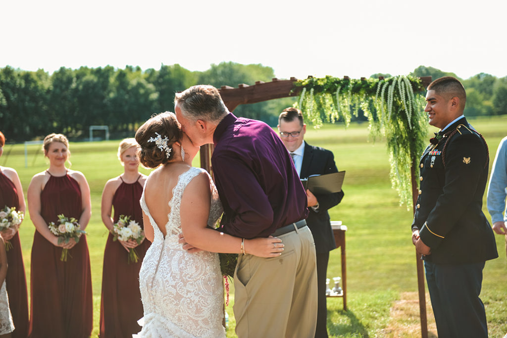 a dad kissing the brides head as he hands her off to the groom