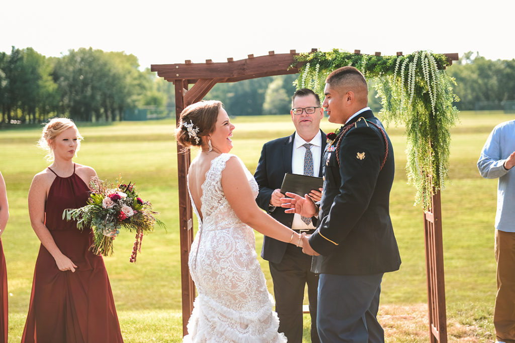 the bride laughing after her first kiss with her groom in front of a wooden arch