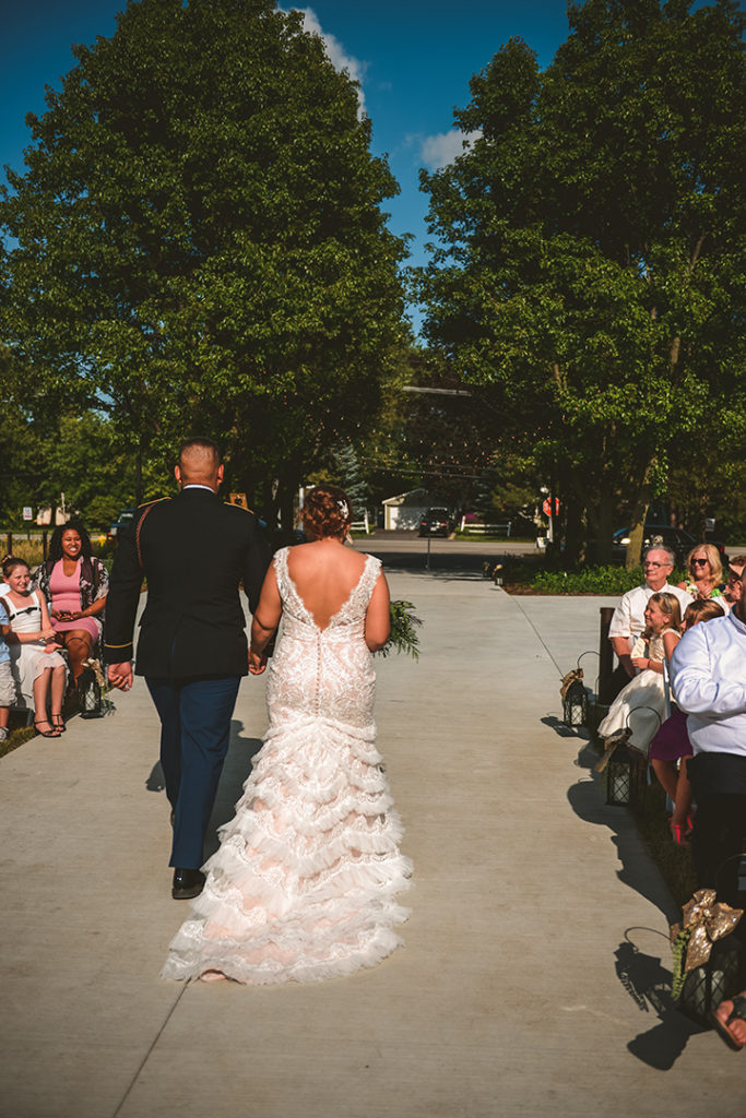 the bride and groom walking away from their family towards tall green trees after their wedding ceremony