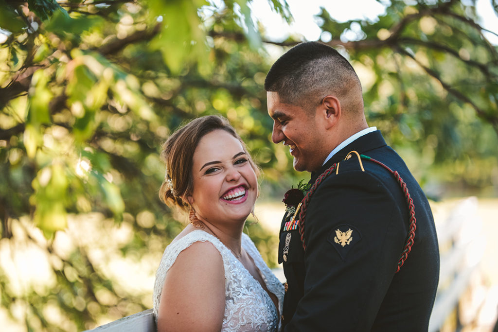 a bride looking at the camera as her husband smile at her in his marine uniform