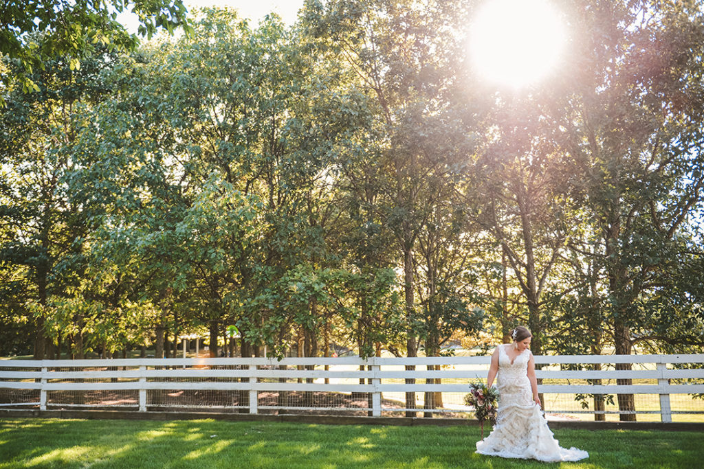a bride adjusting her dress with a sun flair cutting through the trees in the background