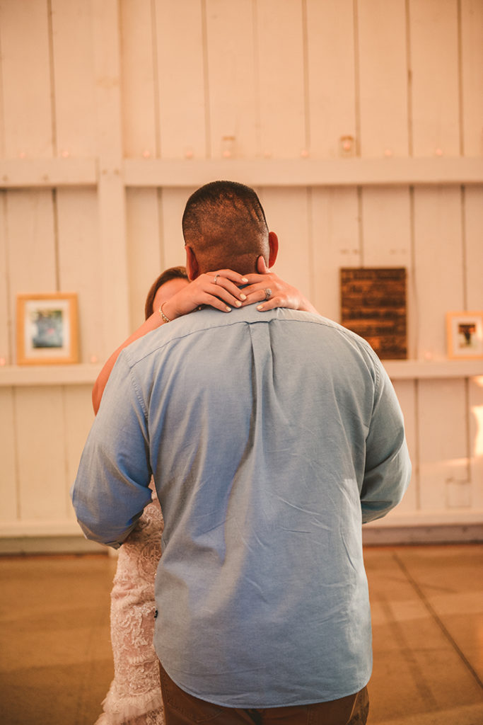 the bride holding onto the groom during their first dance in front of a white wooden wall