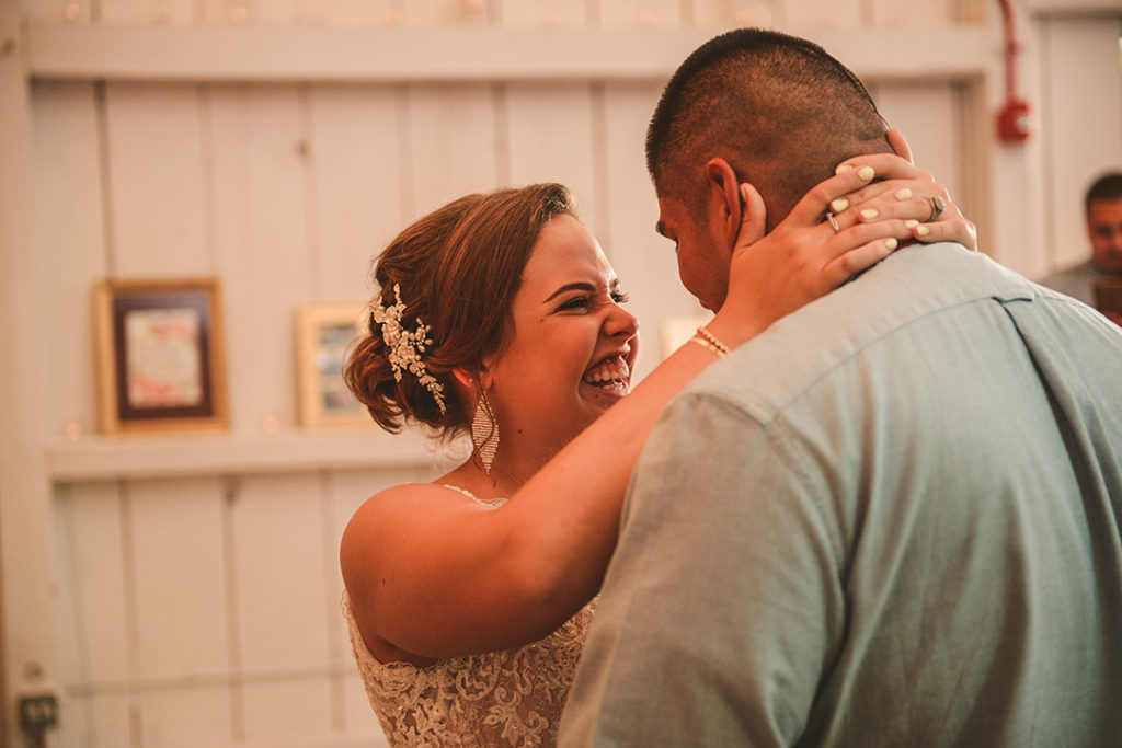 the bride laughing at her husband during their first dance with old white wood walls in the background
