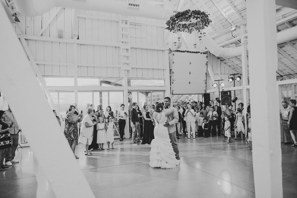 wooden pillars framing the bride and groom during their first dance with their friend and family watching in the background