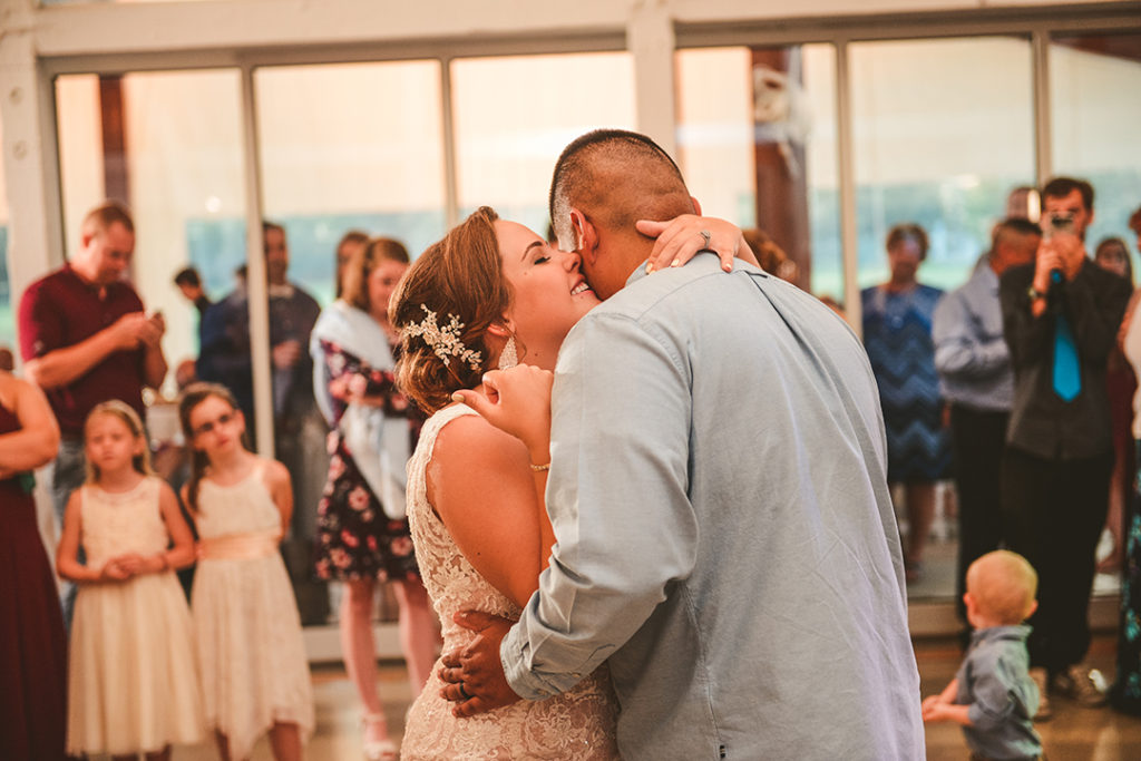 the bride whispering into the grooms ears as their family watches their first dance