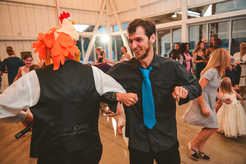 the DJ dancing in a chicken hat with a guest at a wedding reception