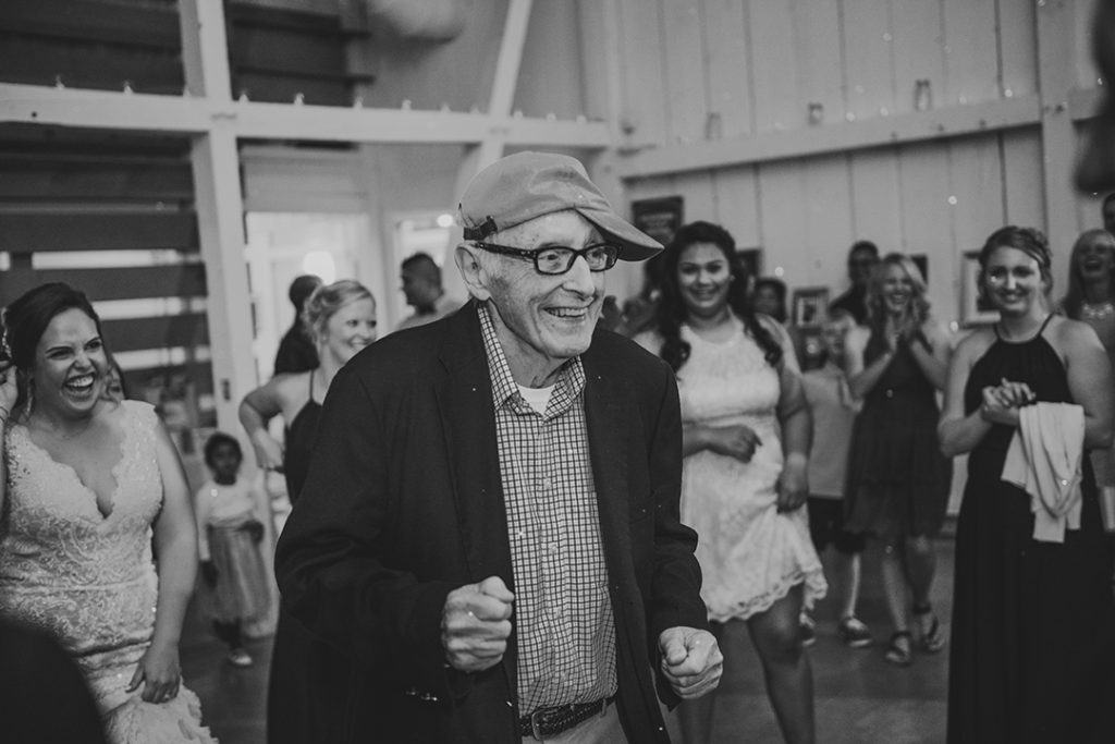 the brides grandfather dancing at a wedding reception as the bride laughs in the background