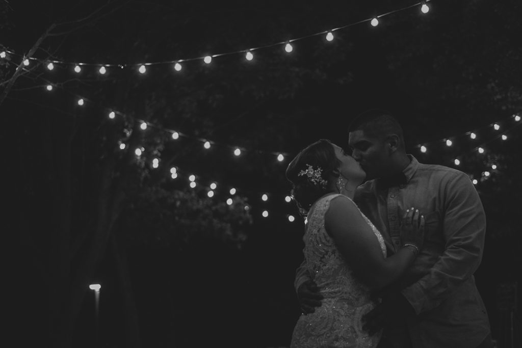 the bride and groom kissing at night under string lights in Olympia fields