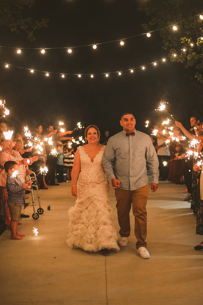 the bride and groom walking towards the camera with their family holding sparklers at night