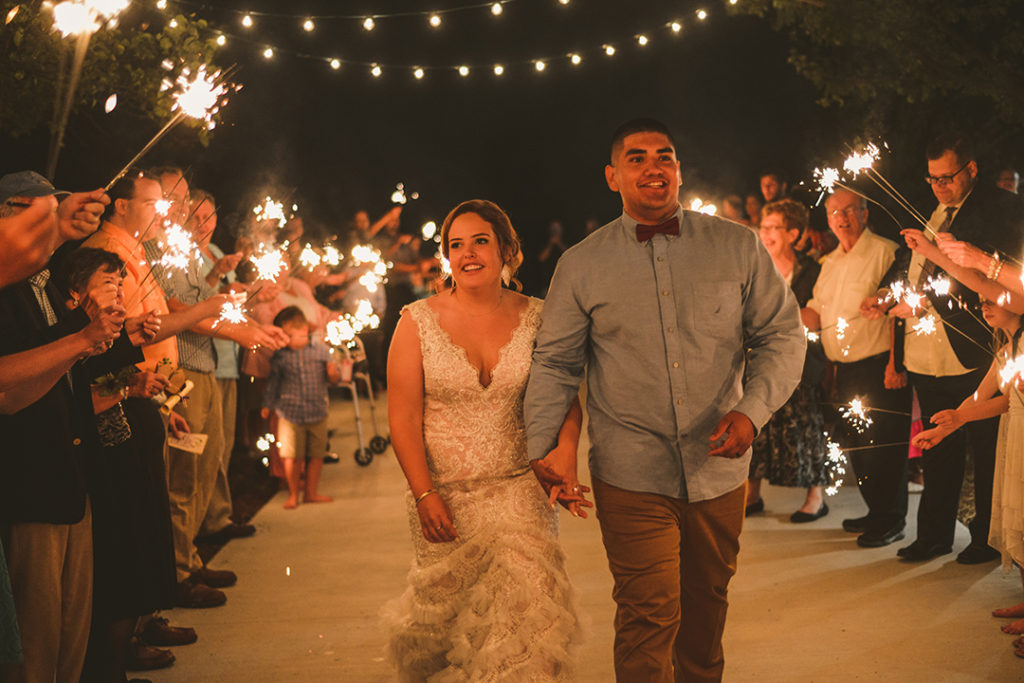 the bride and groom laughing as their family holds sparklers at night in Olympia Fields