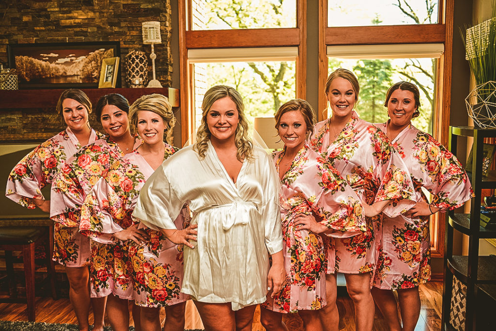 all of the bridesmaids standing in their robes with the bride in a beautifully lit living room
