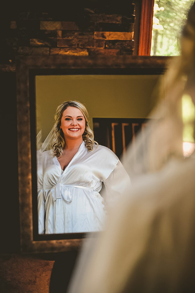 the bride smiling as she looks at herself in the mirror while wearing her robe