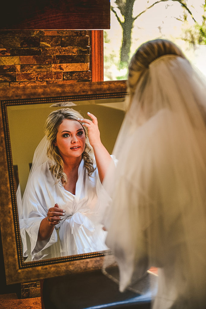 the bride fixing her hair as she looks into a large mirror while in her robe