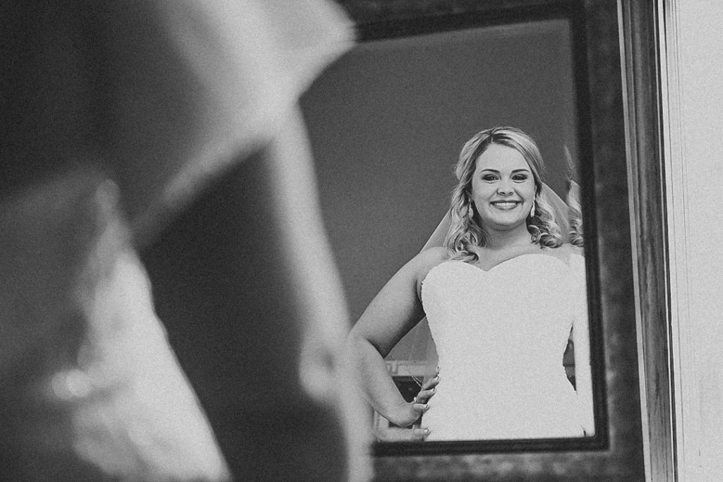 the bride looking into a mirror while smiling in black and white