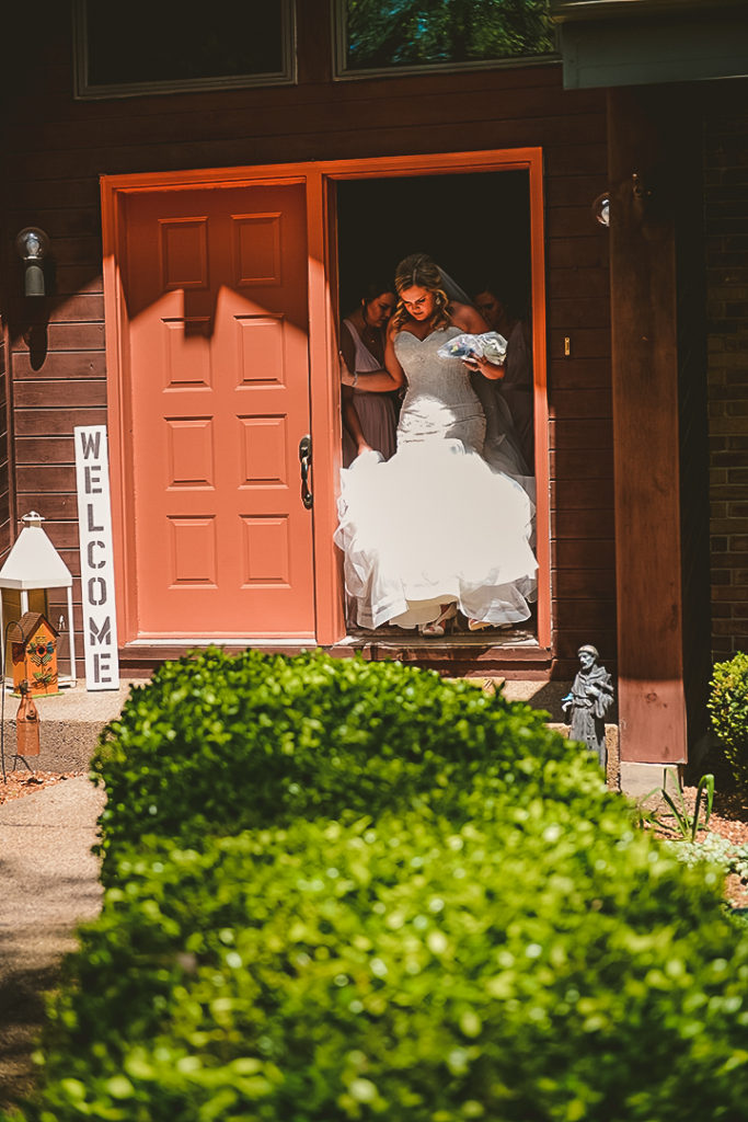 a bride leaving a house with a orange door on a bright summer day