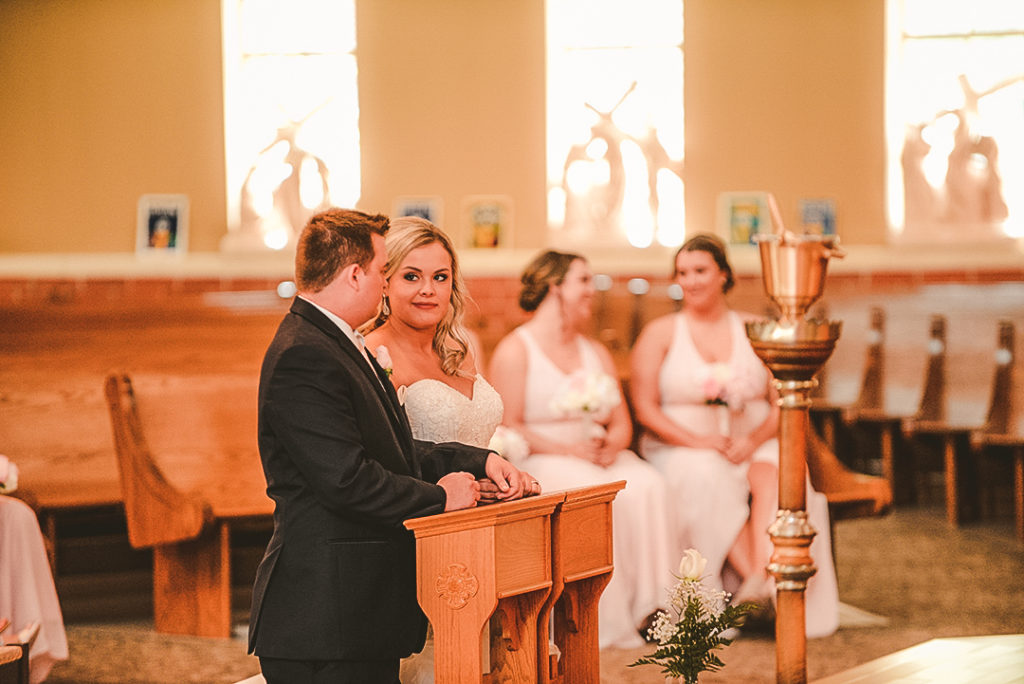 the bride smirking at her groom as they kneel at Morris church