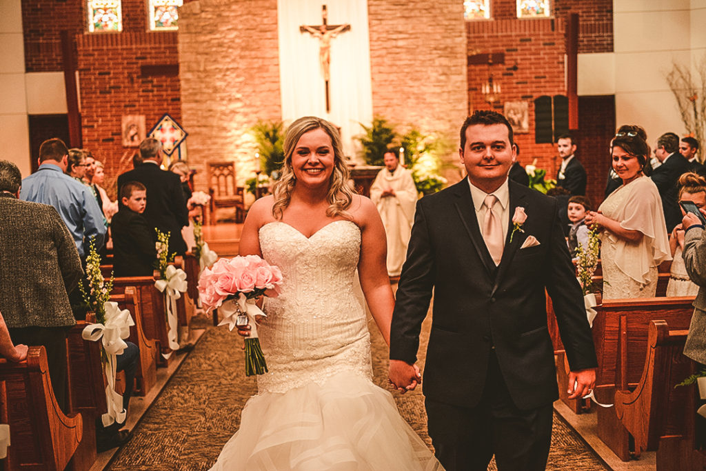 the bride and groom holding hands as they walk down the church aisle after getting married