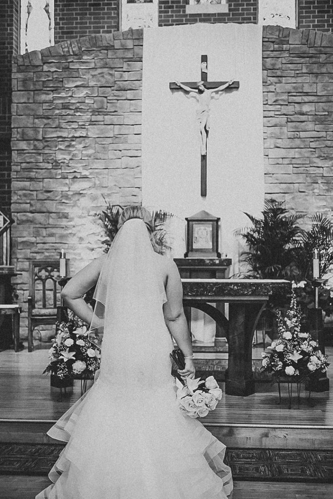 the bride facing the church alter with her hand on her hip in her white wedding dress