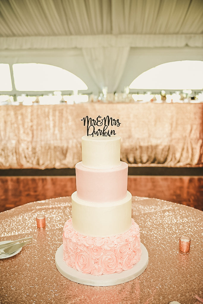 a four tiered cake on a glittery gold table in front of the head table at a Morris wedding reception