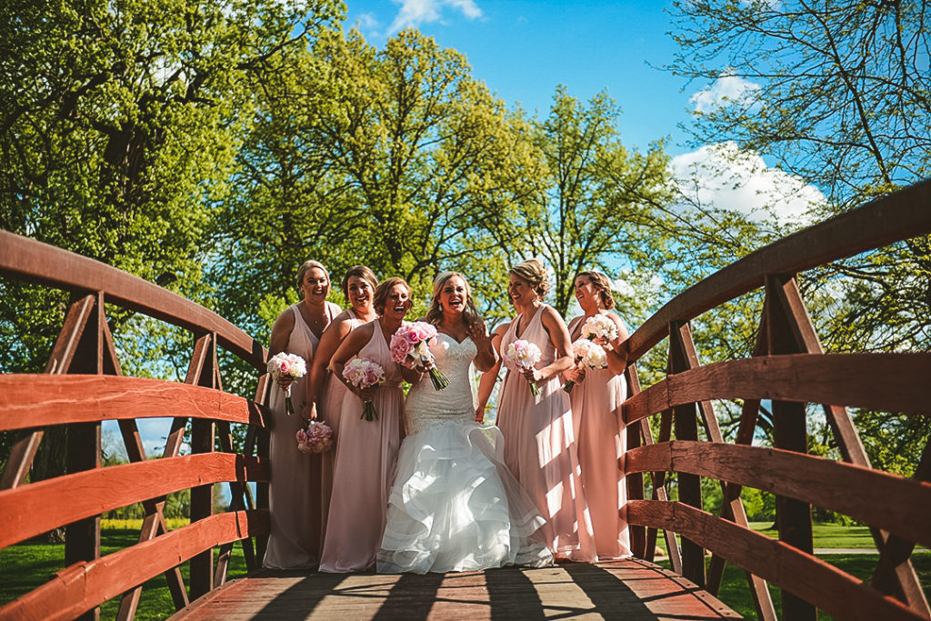 all of the bridesmaids cracking up as they stand on a old bridge