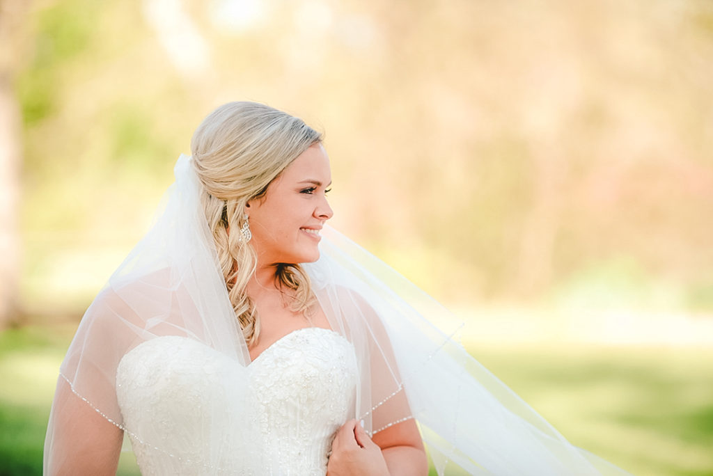 a bride looking out across a golf course as she holds her vail down from the wind